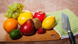 cutting board with fruit such as an orange, apple, lemon, grapes, and others. A cutting knife lies next to it