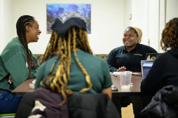 4 BCM students on laptops around a table, laughing