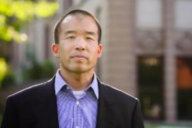 An Asian American man wearing a blazer and purple dress shirt