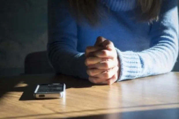 Person seated at table with hands folded next to a smartphone