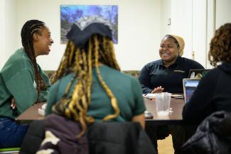 4 BCM students on laptops around a table, laughing