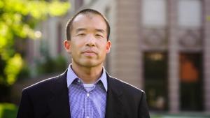 An Asian American man wearing a blazer and purple dress shirt