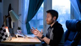 Young male staff sitting at desk having Zoom call on laptop