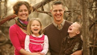 Family photo of mother and father with two small children laughing