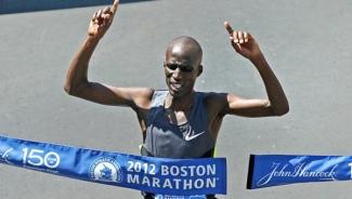 Wesley Korir breaking through tape at Boston Marathon smiling, holding up index finger