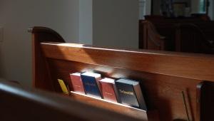 Empty pew with Bibles and hymnbooks in rack