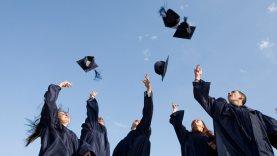 Group of graduates in gowns throwing caps up into air in celebration