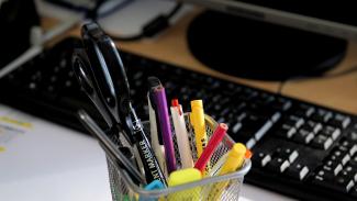 a variety of colorful pens in a cup resting in front of a computer keyboard