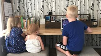 three small children sitting at a countertop using a computer