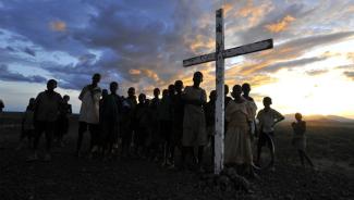 Wooden cross surrounded by group of children with sunset in the background