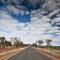 Highway running through rugged landscape with scattered trees and swathes of white clouds