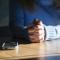 Person seated at table with hands folded next to a smartphone