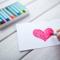 hand coloring a dark pink heart on a small white sheet of paper