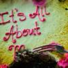 Closeup of pink and yellow cake with "It's All About Me" written in icing. Part of the "Me" has been eaten with a hand and fork poised for more.