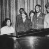 a photo from the 1940's of Black people standing around a piano and singing