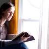 a woman reading a Bible next to a sunlit window